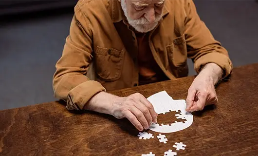 personne âgée entrain de faire un puzzle crâne blanc sur une table